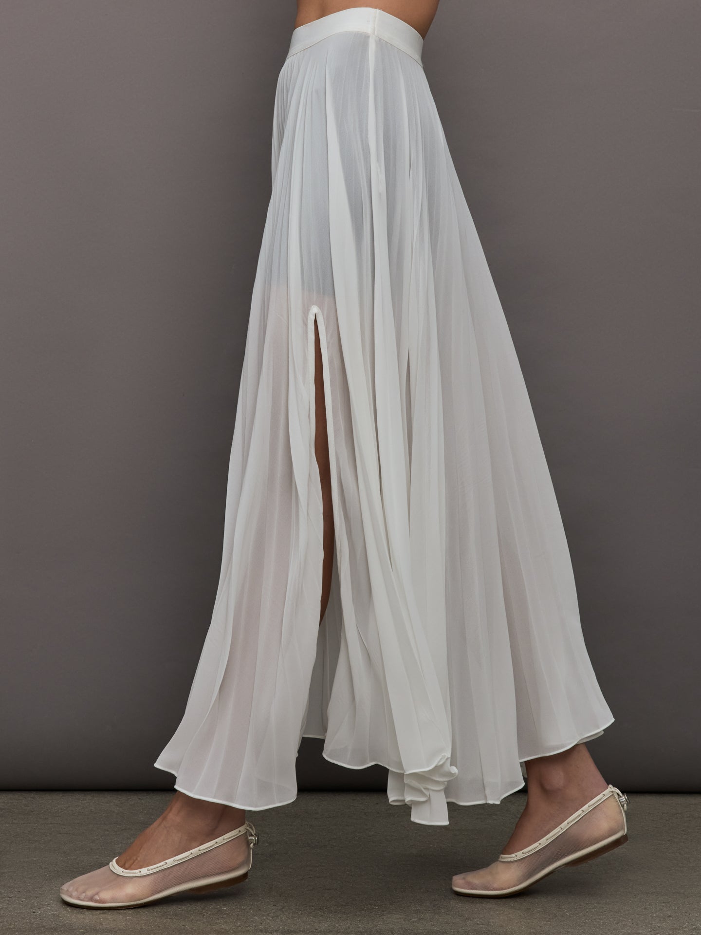 Side view of model wearing Mesh Pleated Skirt Ivory showing pleated drape and slit.
