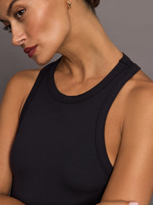 Woman wearing a black ribbed sleeveless dress against a gray background