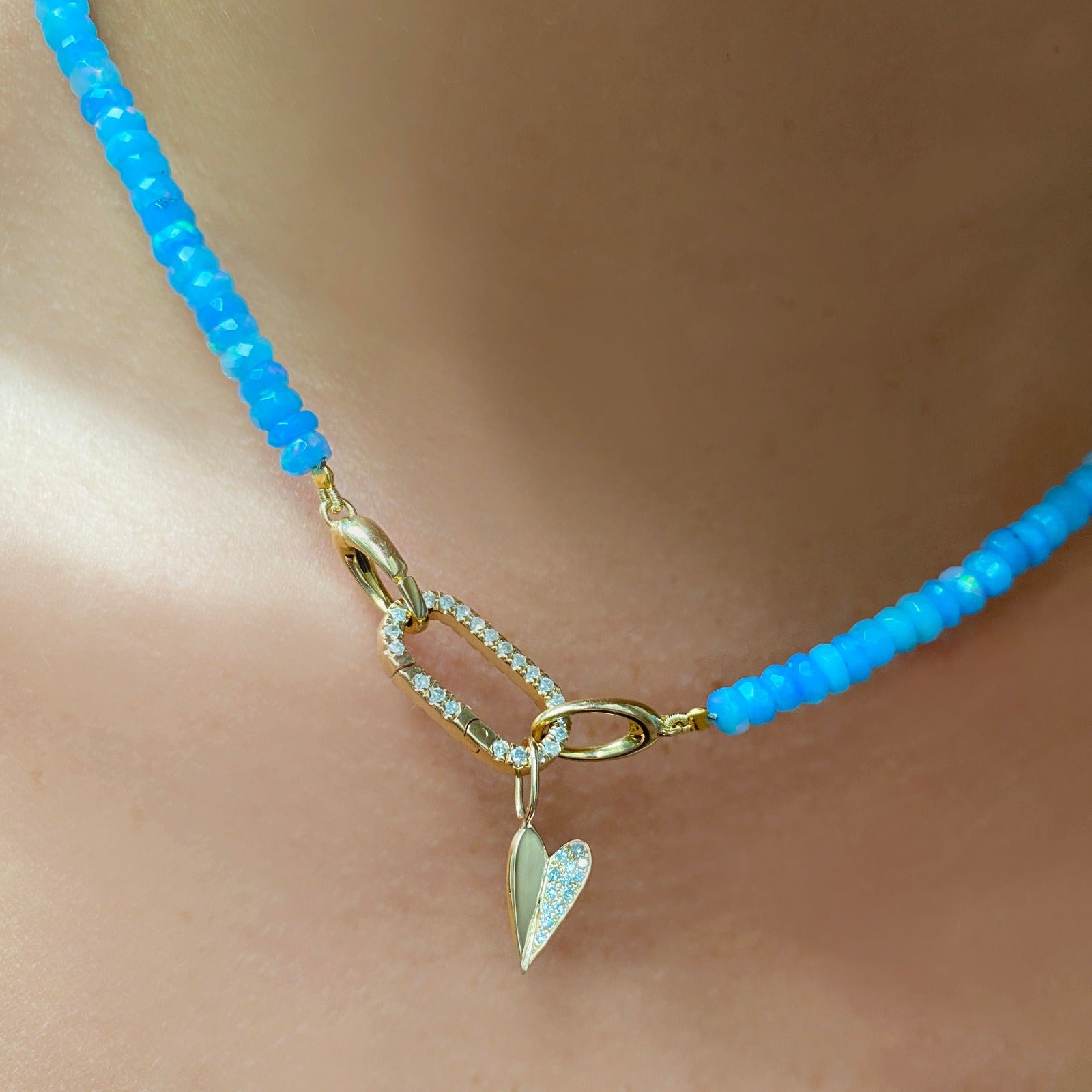 14k yellow gold small folded heart charm with pave diamonds on the right side. Styled on a neck hanging from a medium pave face charm lock, locked onto oval clasps of a beaded necklace.
