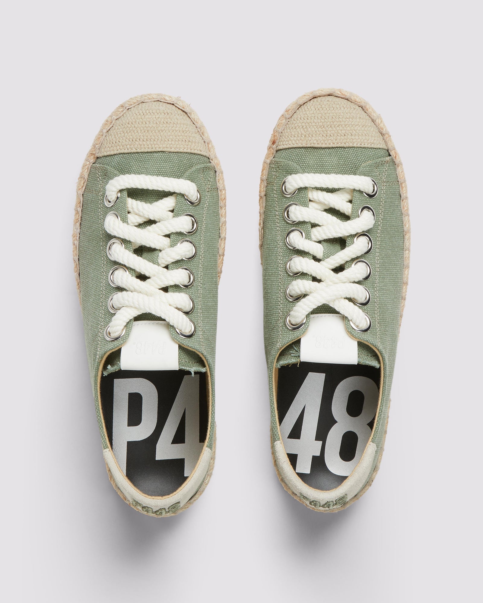 P448 green canvas sneaker with white rope laces and tan recycled suede heel tab, showcasing the organic jute sole and amber rubber tread from a front angle.
