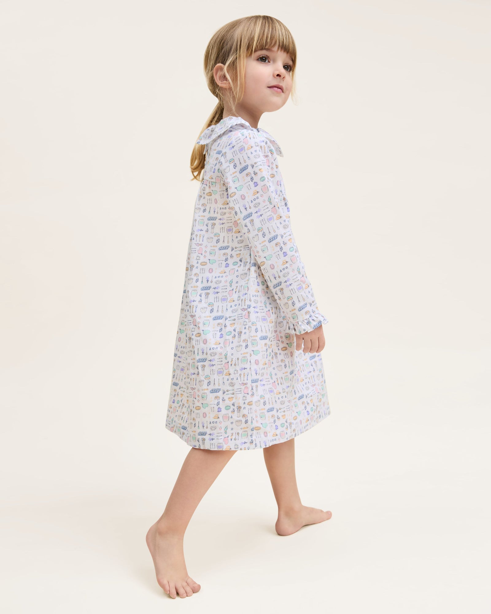 The Kid's Twill Scarlett Nightgown in Baking Spirits Bright features long sleeves, a ruffled collar and cuffs, and a pastel cupcake, teapot, and cutlery print on a white background.