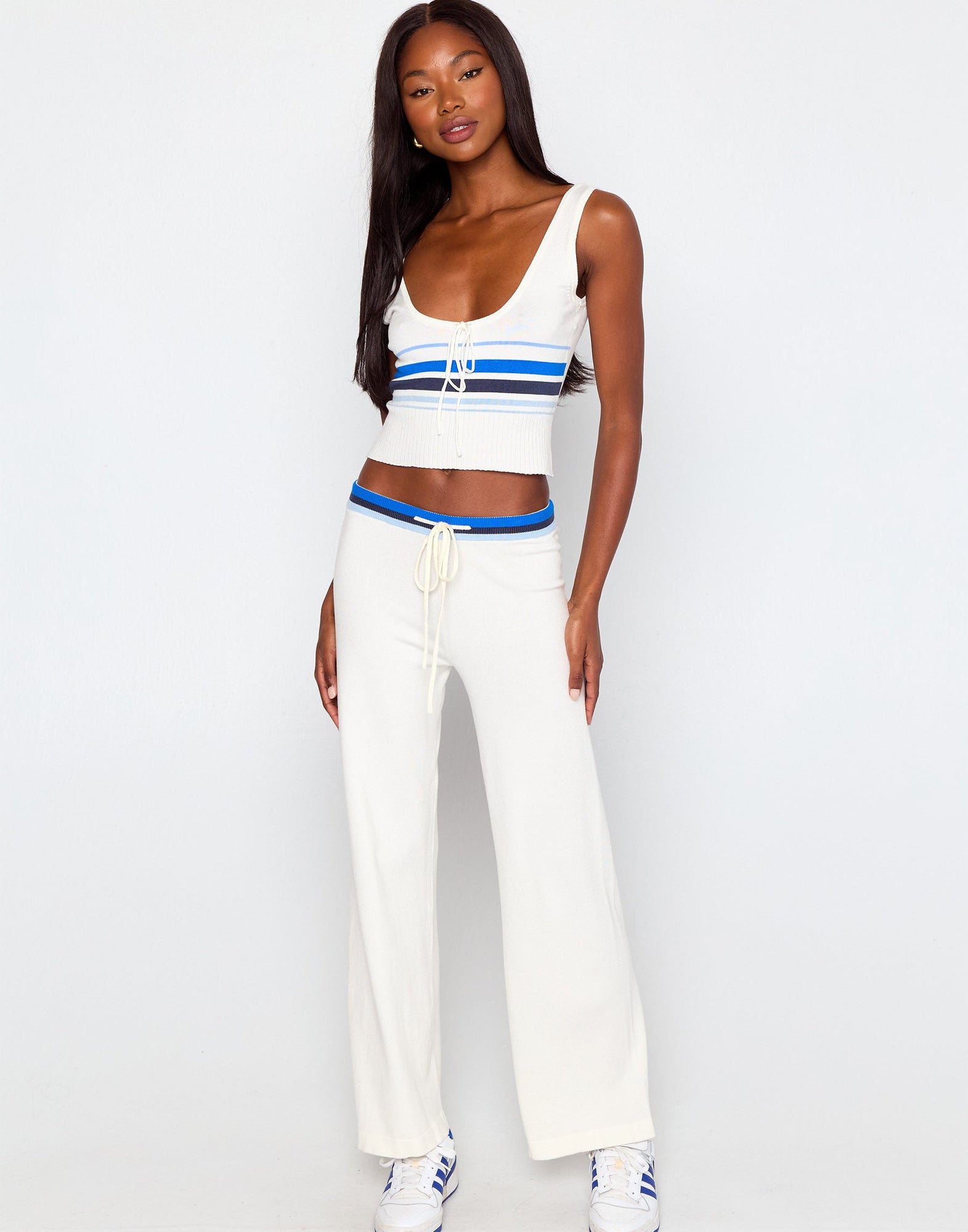 Woman wearing a white sleeveless top with blue accents and white pants on a white background