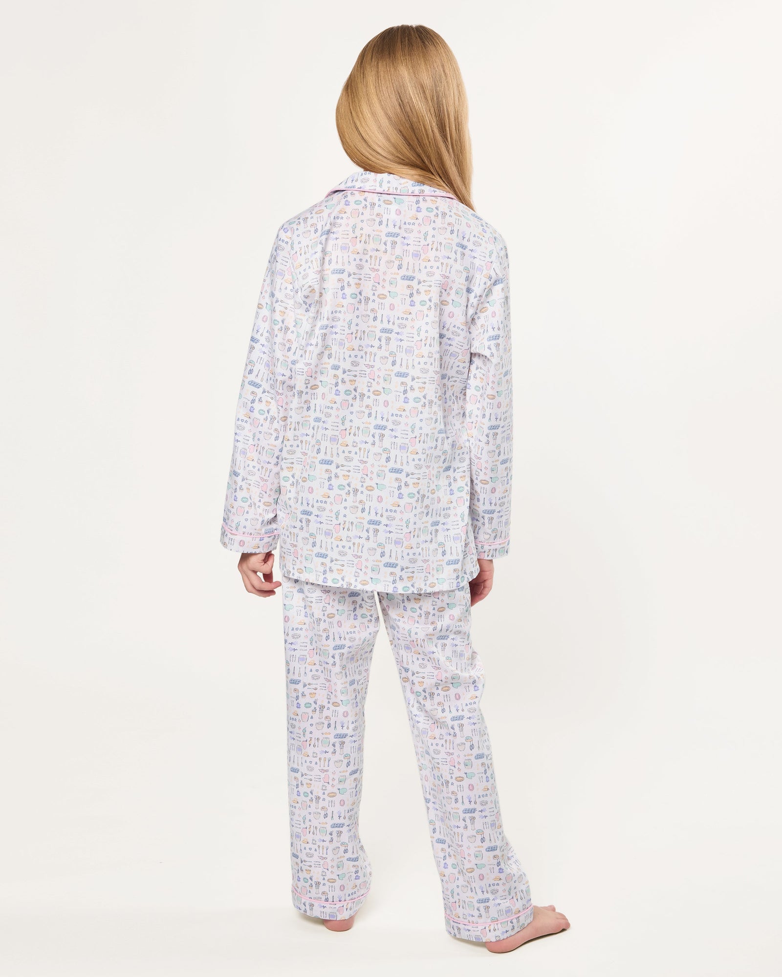 The Kid's Twill Pajama Set in Baking Spirits Bright features white long-sleeve button-up top and long pants with a colorful print of various small household and travel items.