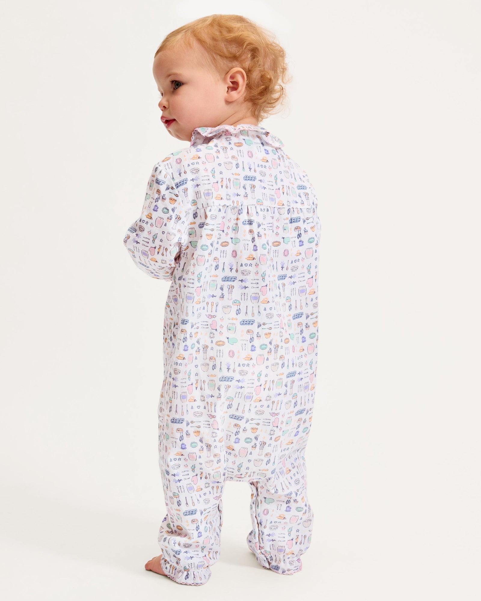 The Baby's Twill Madeline Romper in Baking Spirits Bright features long sleeves, a ruffled collar and cuffs, pastel kitchen print on white, front buttons, and snap closures at the legs for easy dressing.