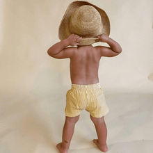 Child wearing yellow and white vertical striped swim trunks, viewed from behind.