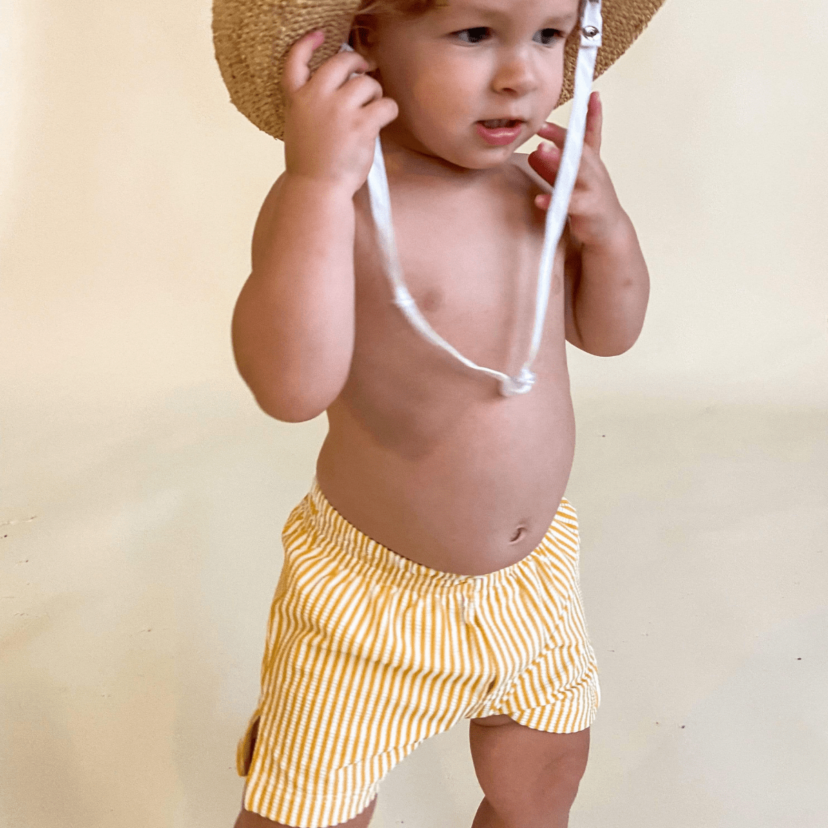 Toddler wearing yellow and white vertical striped swim trunks with white drawstring.