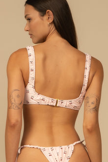 Pink bikini top with cherry print, ruched side straps, and gold center buckle detail, shown from back view.