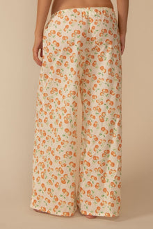 Cream-colored wide-leg pants with orange cherry print and drawstring waist, shown from behind on model.