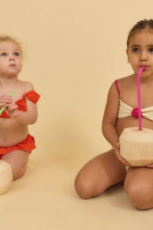 Two children wearing bikini sets with cream-colored bases and contrasting trim details in red and pink.