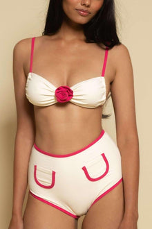 Cream bikini bottom with raspberry binding trim and decorative U-shaped pocket details.