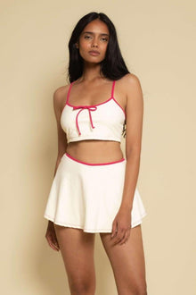 Cream racerback sport top with raspberry binding and drawstring detail, paired with matching cream skirt with raspberry trim.