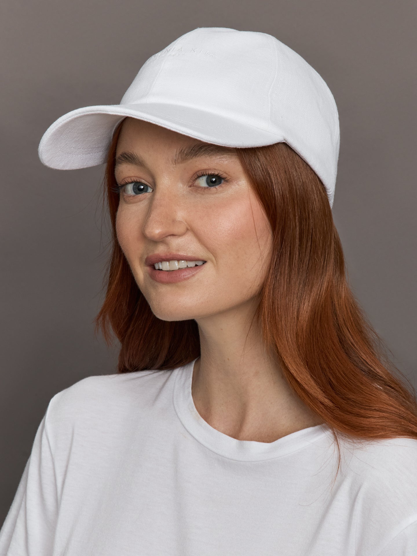 Model wears white linen baseball cap with an embroidered logo on the front and a ruched elastic back.