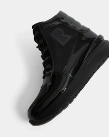 The Rudsak CHELSA - L224505 Black is a women’s black high-top sneaker boot with glossy and matte finishes, black laces, a bold “R” side logo, and a waterproof zipper. Shown angled to reveal the side and sole against a white background.