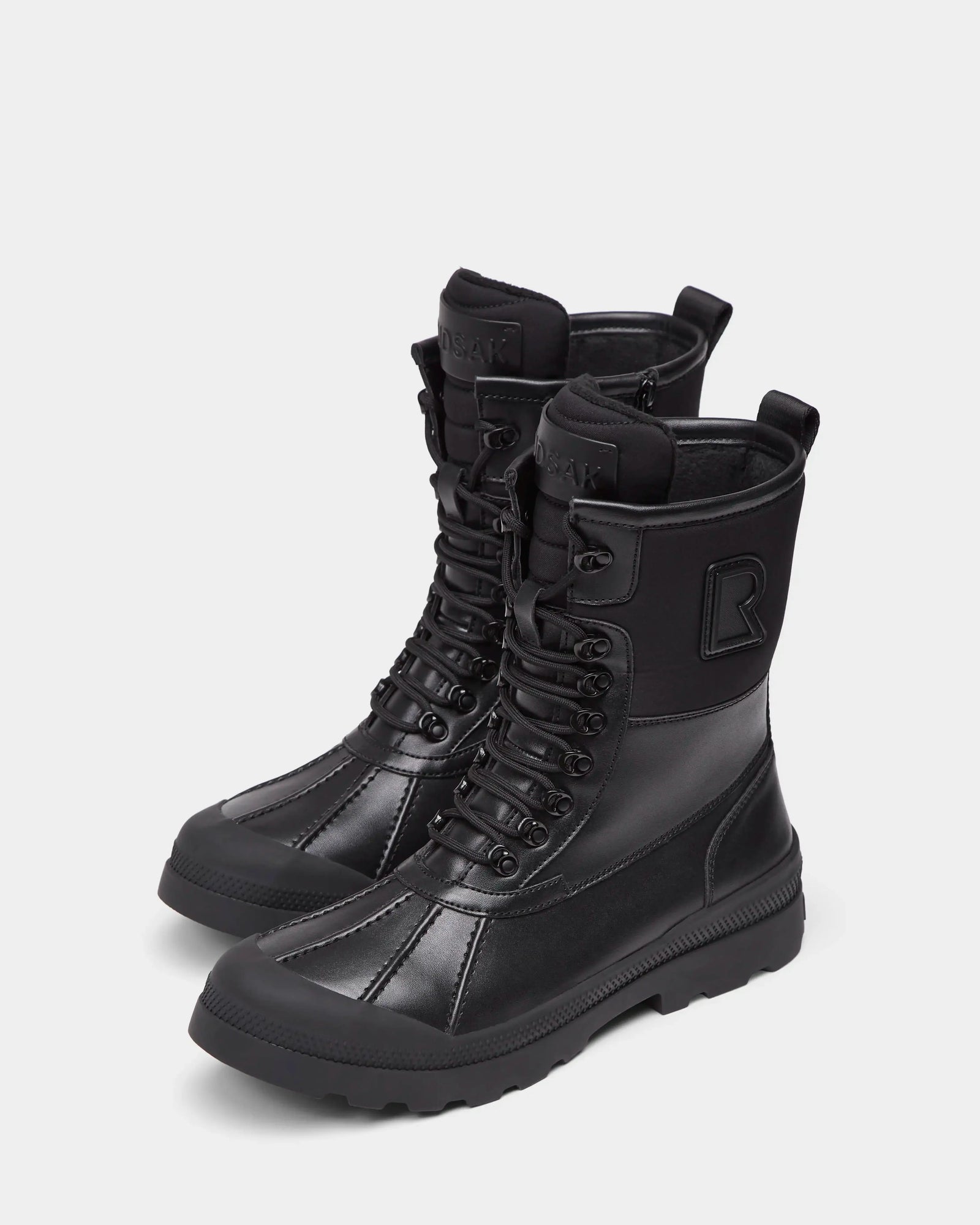 The DAMIEN - M222500 Black by Rudsak are men's high-top winter boots in black, crafted from weather-treated leather with rugged soles, side zippers, stitched panels, and a raised R logo on the outer sides.