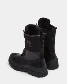 A pair of Rudsak DAMIEN - M222500 black men’s winter boots with insulated design, textured soles, side zippers, and bold RUDSAK branding on the back heel and sides, shown on a light gray background.