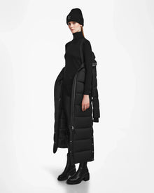A person models the Rudsak IZABELLA - L124541 Black quilted maxi coat over a black turtleneck, pants, boots, and beanie, presenting this winter essential against a plain white background.