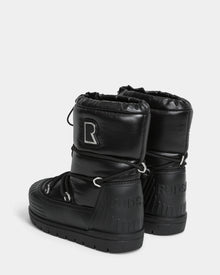 The KIKA - L224506 Black by Rudsak are shiny black winter boots with chunky rubber soles, a large R patch on one boot, Rudsak embossed on the heels, drawstring closures, and stylish rubber detailing.