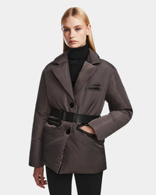 A woman with straight blonde hair wears the Rudsak PAOLA - 8124547 Grey womens down blazer over a black turtleneck and black pants, standing against a plain white background.