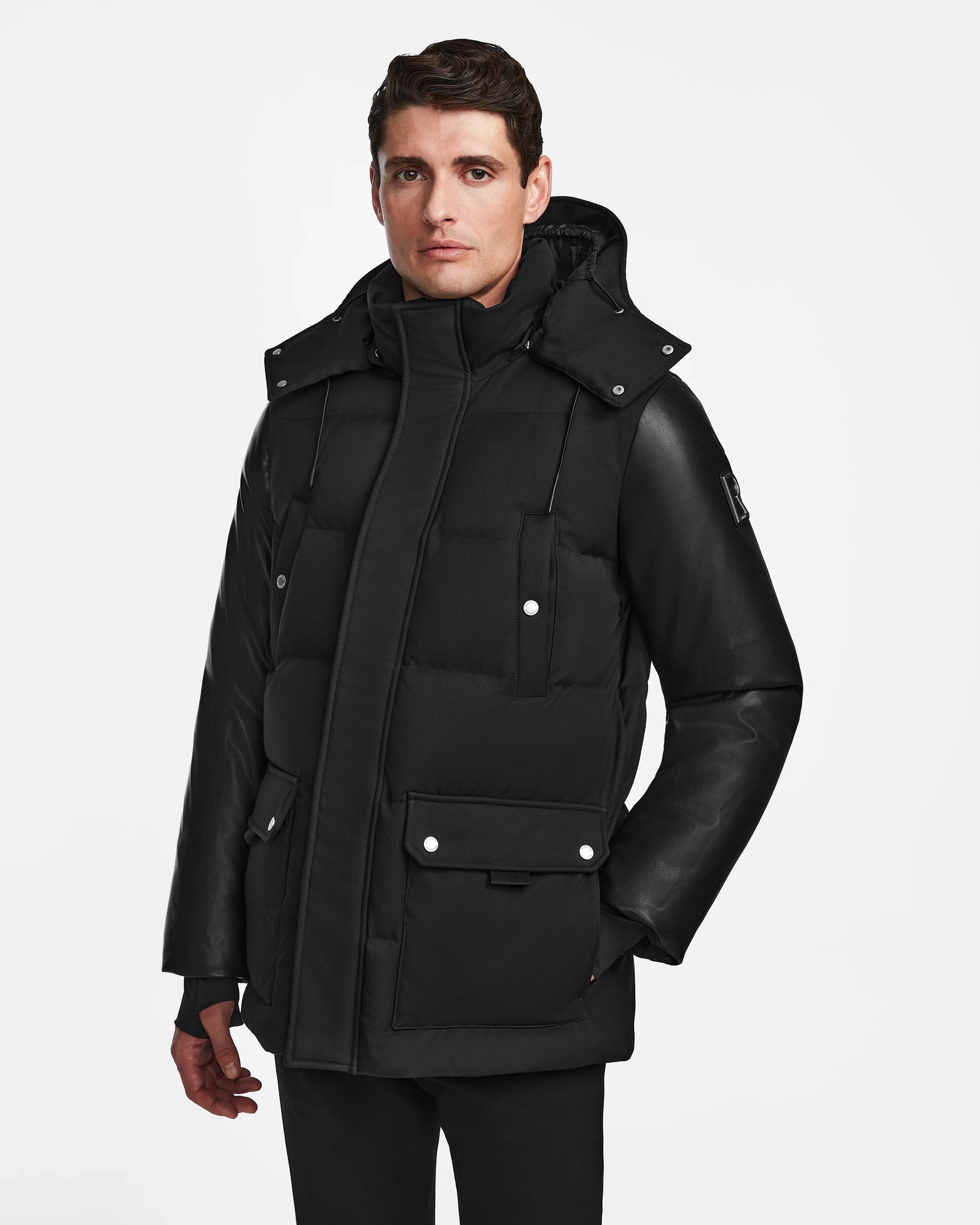 A man wearing the Rudsak RICKY R - M123506 Black parka with recycled leather sleeves and multiple pockets stands against a plain white background.