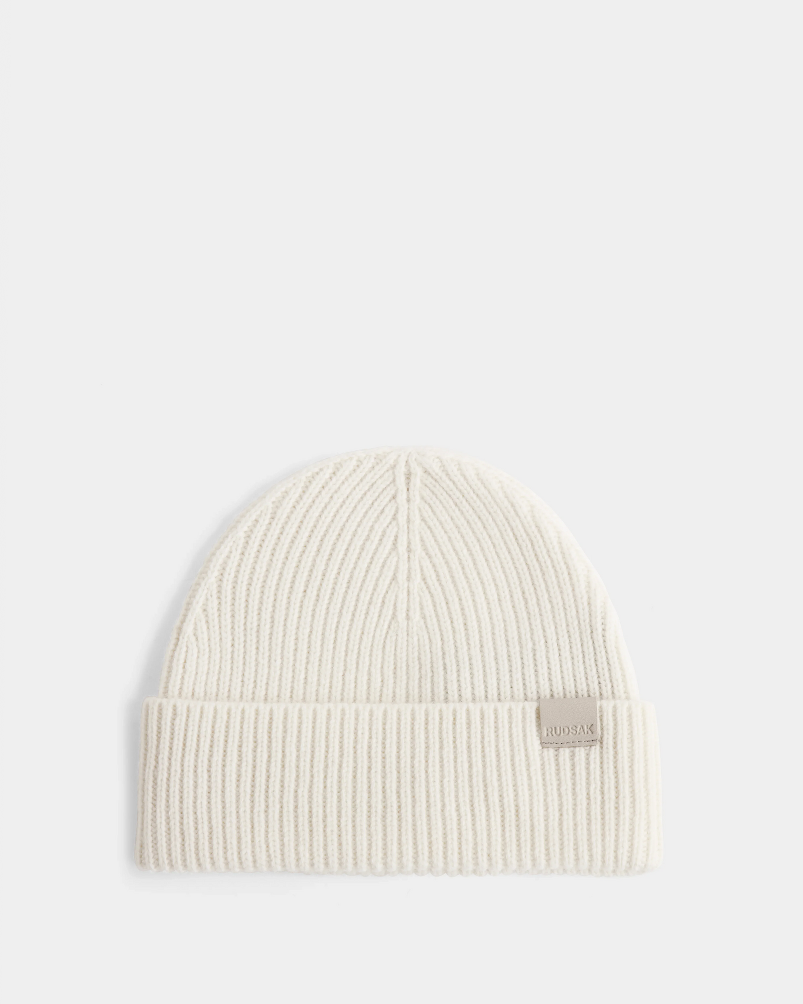 The Rudsak ANDREY - U425507 Vanilla is a cream rib-knit hat with a folded brim and a small rectangular front tag, shown on a plain white background.