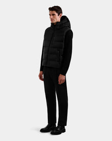 A man stands against a plain background wearing the Rudsak BROOKS - M125520 Black men’s down puffer vest over a black long-sleeve shirt, black pants, and black shoes. He faces slightly right with arms relaxed at his sides.