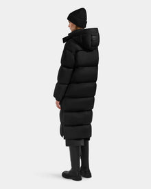 A person wearing the Rudsak KARLEE XL - 8125683 Black long maxi down puffer jacket stands facing away and slightly to the side against a plain light gray background—a true winter essential.