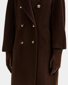 A person wears the MARINE - 8424516 Espresso long double-breasted coat with ribbed knit cuffs, paired with dark brown Rudsak gloves. The image focuses on the torso and arms.