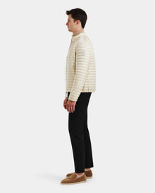 A man stands in profile against a white background, wearing the Rudsak REYMOND M - M125523 Vanilla recycled nylon men’s down jacket, paired with black pants and tan loafers.