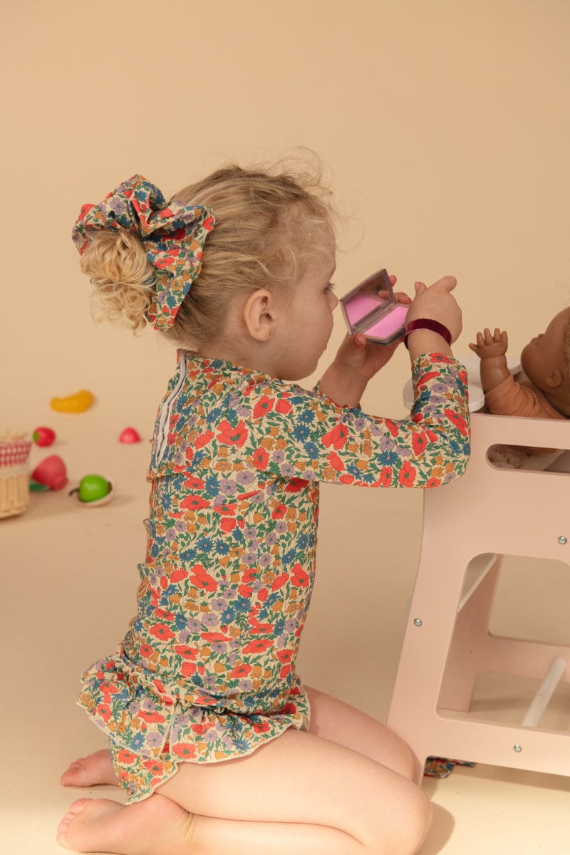 Toddler wearing colorful floral long-sleeve rashguard with red, orange, and blue flowers on cream background.