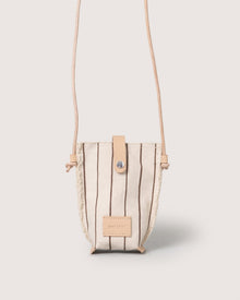 A compact, beige Graf Lantz Hana Canvas Phone Crossbody with vertical brown stripes, tan leather strap and snap closure, plus a front tan leather patch—shown against a light background for stylish hands-free convenience.