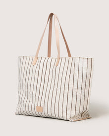 The Graf Lantz Hana Boat Bag is a spacious, cream canvas tote with thin brown stripes and two tan leather handles, shown standing upright against a light background.