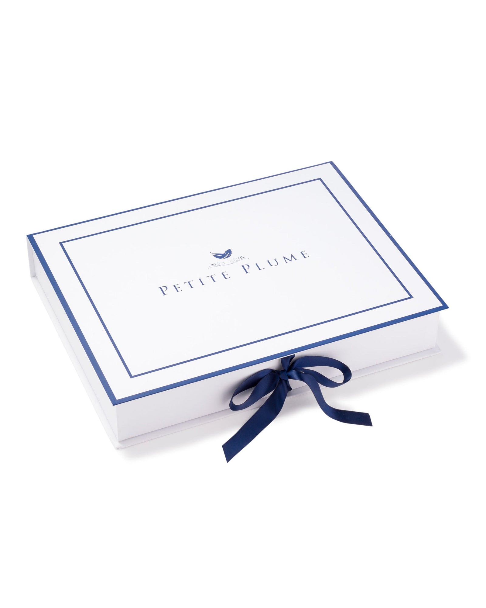 A rectangular white box features Petite Plume centered, bordered by a thin blue line, adorned with a blue bow and a small bird icon above the text. Perfect for encasing Kids Delphine Slipper in Black Velvet, it offers luxurious comfort for pampering little feet.