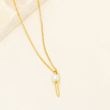 Gold and Pearl Golf Tee Necklace on Tan Background