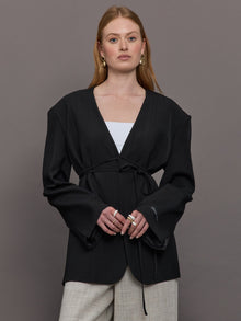 Model wears a wide shoulder black blazer with a deep v neck and drawstring closure. 