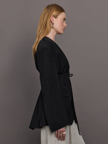 Model wears a wide shoulder black blazer with a deep v neck and drawstring closure. 