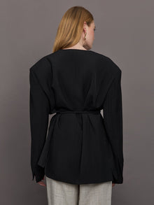 Model wears a wide shoulder black blazer with a deep v neck and drawstring closure. 
