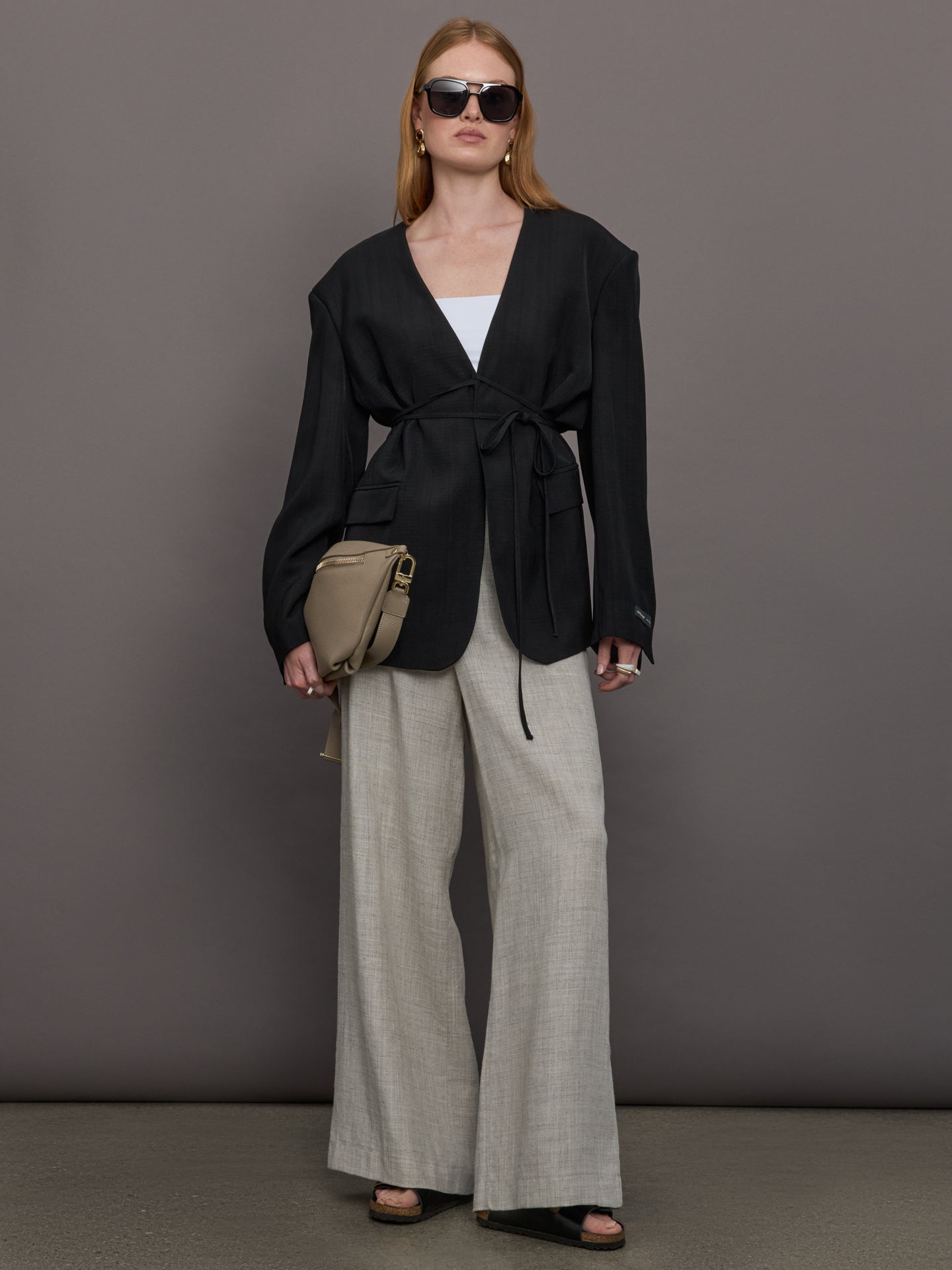 Model wears a wide shoulder black blazer with a deep v neck and drawstring closure. 