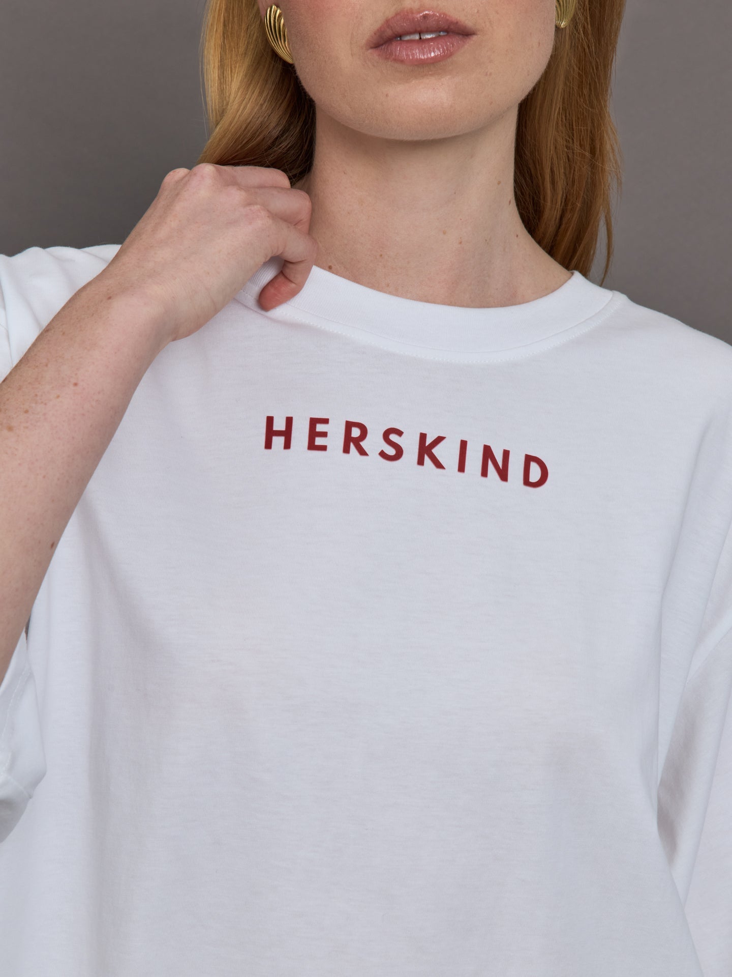 Model wears an oversized wide sleeve white tee shirt with red Herskind lettering across the chest.