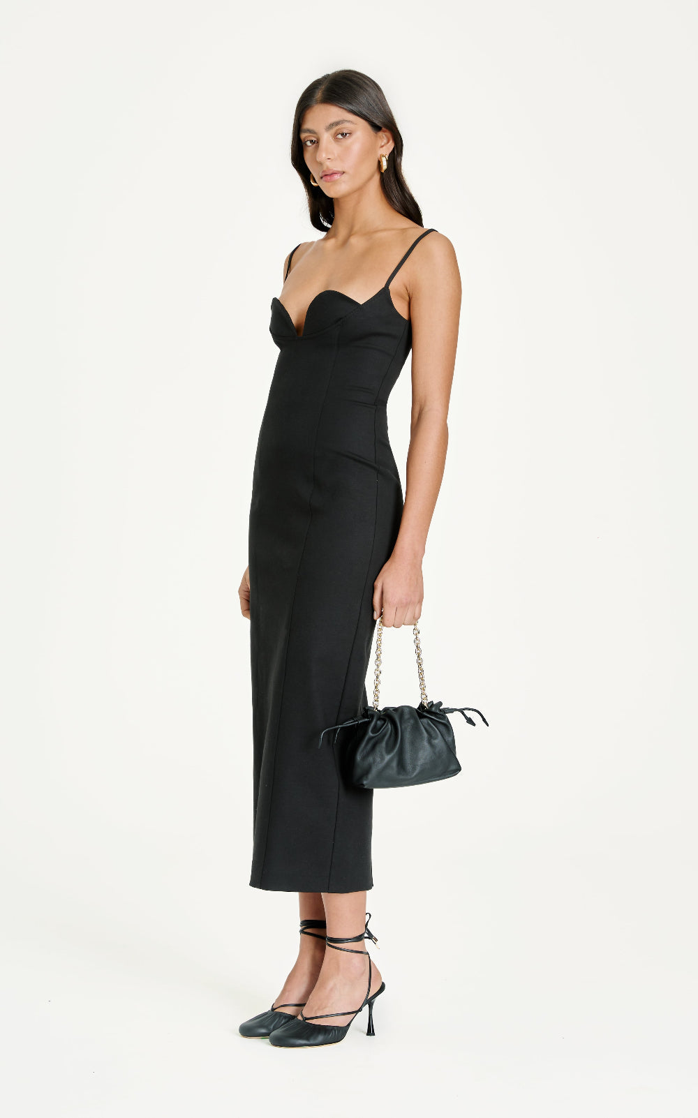 Woman wearing a black dress holding a matching handbag on a white background