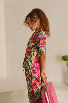 Woman wearing short-sleeved top with multicolored floral print in pink, red, green, and yellow on cream background.