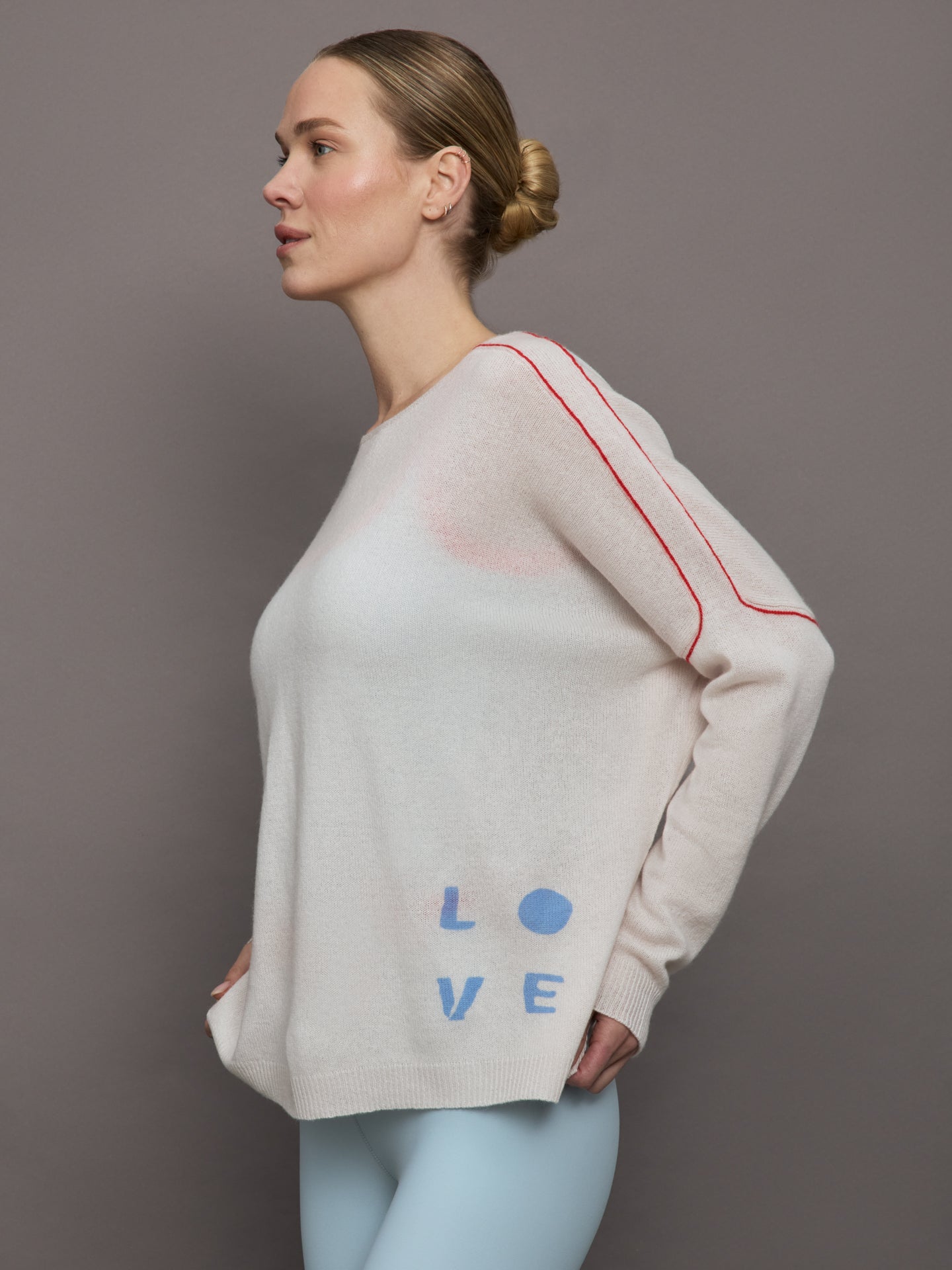 Model wears a white sweater with red seams along the biceps and blue block lettering on front bottom right that says LOVE. Back of sweater says in blue lettering "Love is all around you."