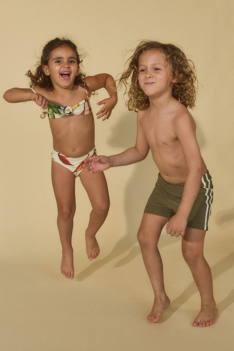 Child wearing khaki and white patterned swim shorts with white stripe detail on the side.