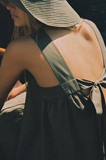 Khaki Hannah dress with open back and tie detail, shown from rear on model wearing straw hat.