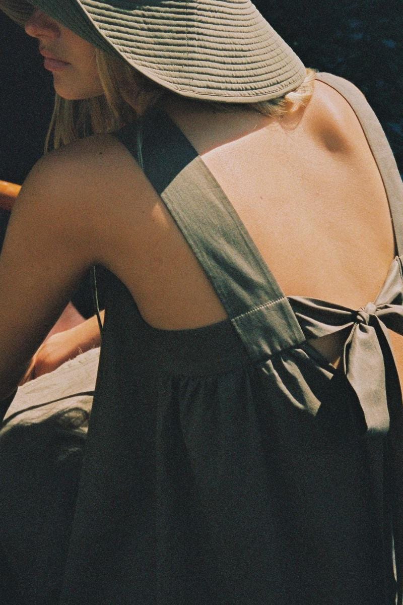 Khaki Hannah dress with open back and tie detail, shown from rear on model wearing straw hat.