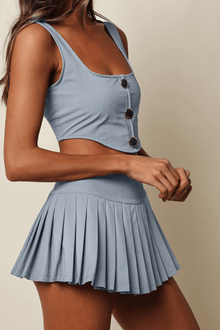 Light blue denim sleeveless crop top with button details and matching pleated tennis skirt.