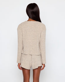 Woman wearing a beige ribbed knit loungewear set including a cropped tank top, drawstring shorts, and a matching button-up cardigan with long sleeves, posing against a plain white background.