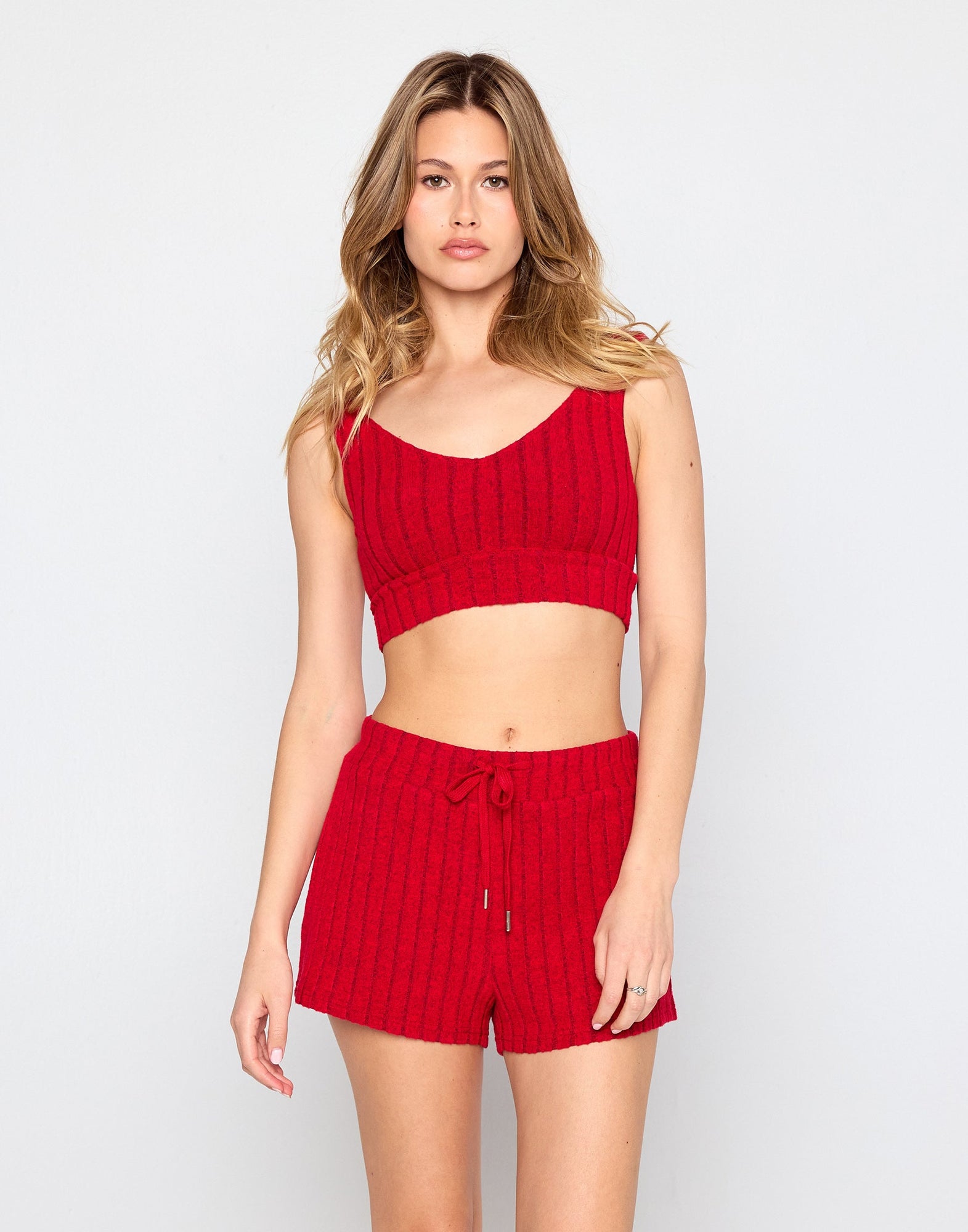 Woman wearing a cozy, red ribbed knit lounge set consisting of a cropped tank top and matching high-waisted drawstring shorts