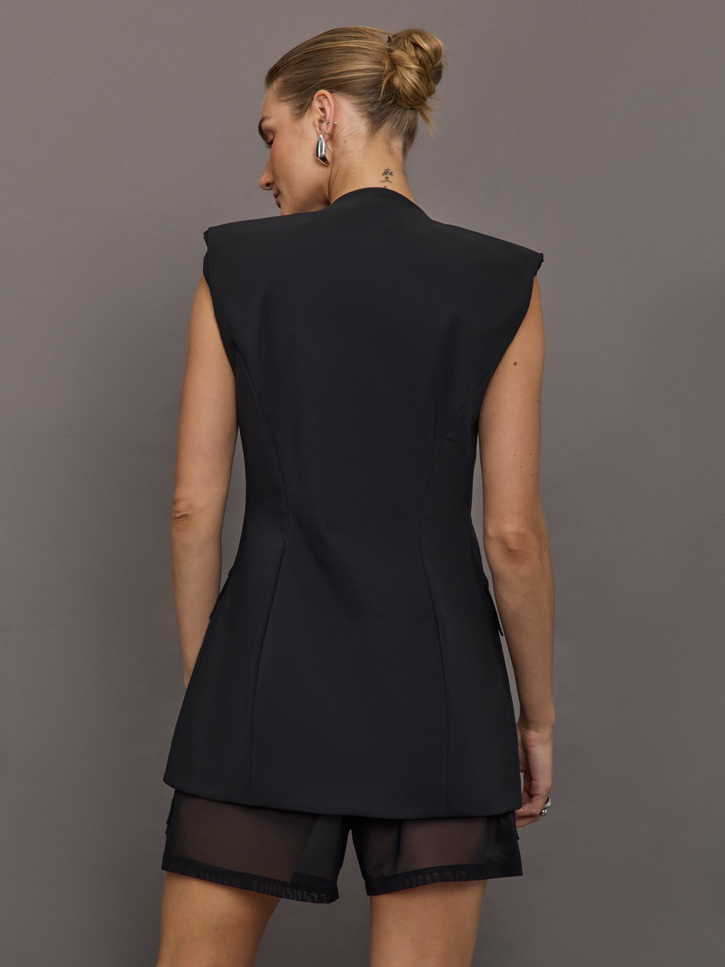 Model wears black Odyssey Vest with a silver front zip, pockets and a v-neckline.