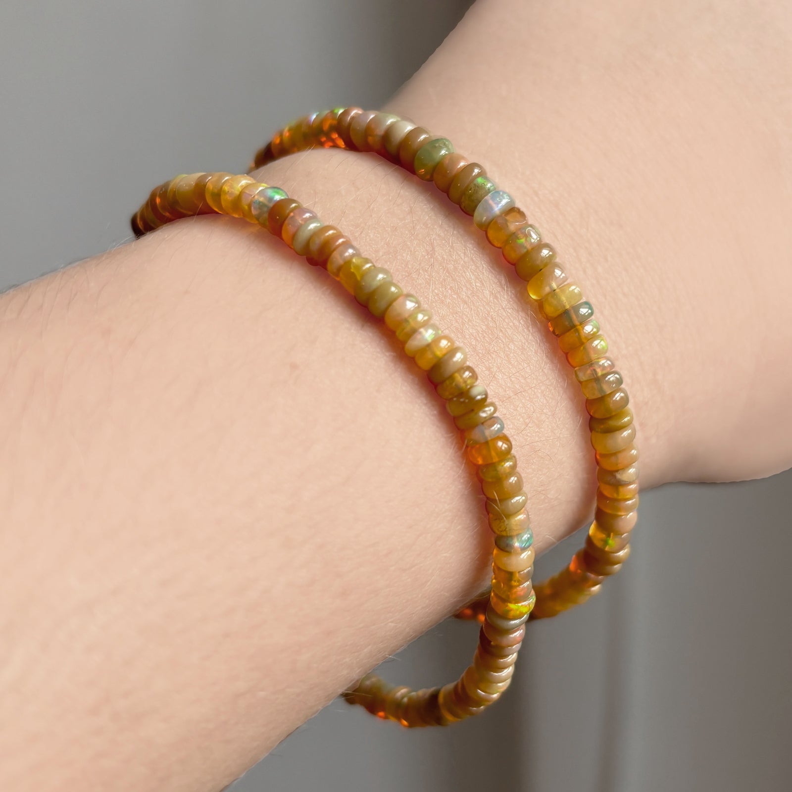 Shimmering beaded bracelet made of smooth opals in shades of light brown and light orange on a gold linking lobster clasp styled on a wrist