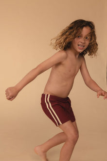 Maroon swim trunk with white side stripes on child model.